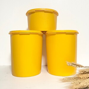 May include: Three yellow plastic storage containers stacked on top of each other. The containers are round and have a smooth surface.