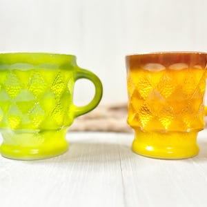 May include: Two vintage glass mugs with a geometric pattern. The mug on the left is green and the mug on the right is yellow.