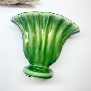 May include: A green ceramic vase with a ruffled top and a round base. The vase has a glossy finish and is shaped like a flower.
