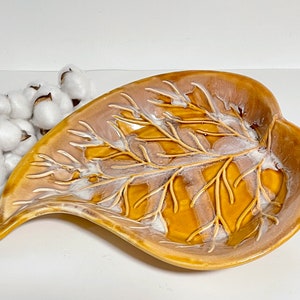 May include: A ceramic leaf-shaped dish with a brown glaze and a white raised design of branches. The dish is ideal for serving snacks or holding small items.