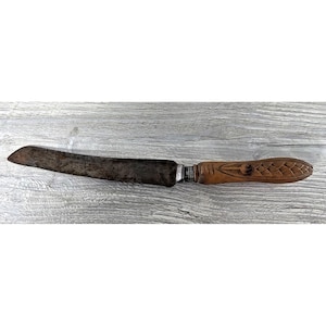 May include: A vintage knife with a dark, aged blade and a carved wooden handle. The handle features a detailed design, and the blade shows signs of wear, suggesting its use over time. The knife rests on a wooden surface.