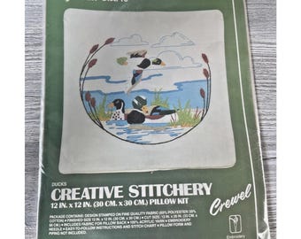 May include: A vintage Vogart Crafts pillow kit featuring a duck design. The kit includes fabric, yarn, and instructions for a 12 x 12 inch (30 x 30 cm) pillow. The package is green and white with the words "Creative Stitchery" and "Ducks".