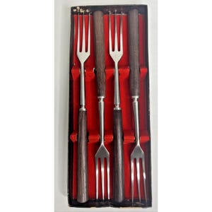 Può includere: Set di quattro forchette da fonduta con rebbi in acciaio inossidabile e manici in legno scuro. Le forchette sono esposte in una scatola foderata di velluto rosso con esterno nero. Utensile da cucina vintage.