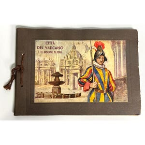 Puede incluir: Un álbum de fotos marrón vintage con una ilustración a color de un guardia suizo con uniforme sosteniendo una alabarda, con la Ciudad del Vaticano y la Basílica de San Pedro al fondo. La portada del álbum tiene el texto "CITTA DEL VATICANO E LE BASILICHE DI ROMA".