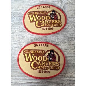 Puede incluir: Dos parches bordados ovalados con fondo beige y borde rojo. El texto dice 25 YEARS LONG ISLAND WOOD CARVERS ASSOCIATION 1974-1999. Cada parche presenta una ilustración bordada de una persona tallando madera con una camisa de color rojo.