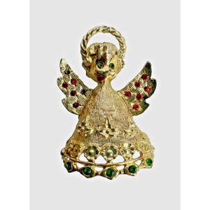 May include: Gold-toned angel pin with a textured finish. The angel has a halo, wings, and a dress, all adorned with red and green gemstones. The angel's eyes are green. A decorative accessory.