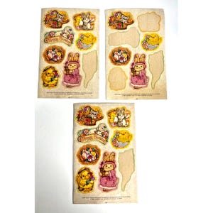 May include: Three sheets of vintage Easter stickers. Each sheet features colorful illustrations of bunnies, chicks, cats, and floral baskets. The stickers have a pastel color palette and include the text "Happy Easter".