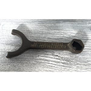 May include: A vintage Champion Brass wrench with a dark brown finish. The wrench has a curved end and a hexagonal socket. The text "CHAMPION BRASS LOS ANGELES CALIF" is embossed on the tool.