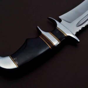 May include: A black and silver hunting knife with a black handle and gold accents. The blade has a serrated edge and a pointed tip.