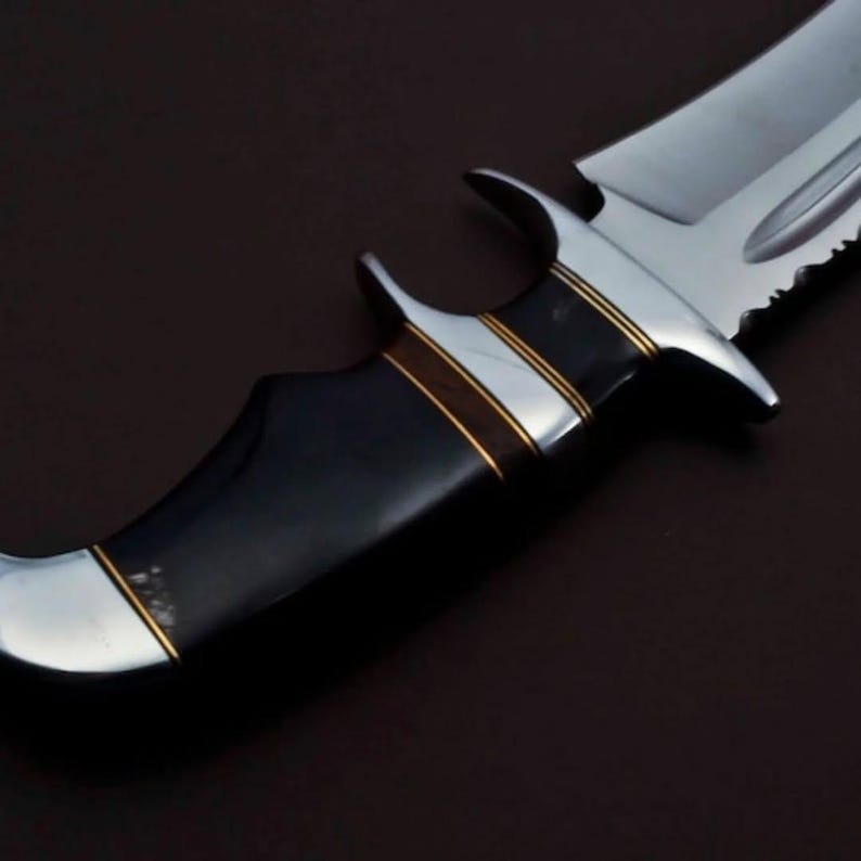 May include: A black and silver hunting knife with a black handle and gold accents. The blade has a serrated edge and a pointed tip.