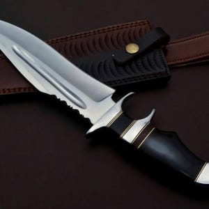 May include: A silver knife with a black handle and gold accents. The knife has a serrated edge and a leather sheath.