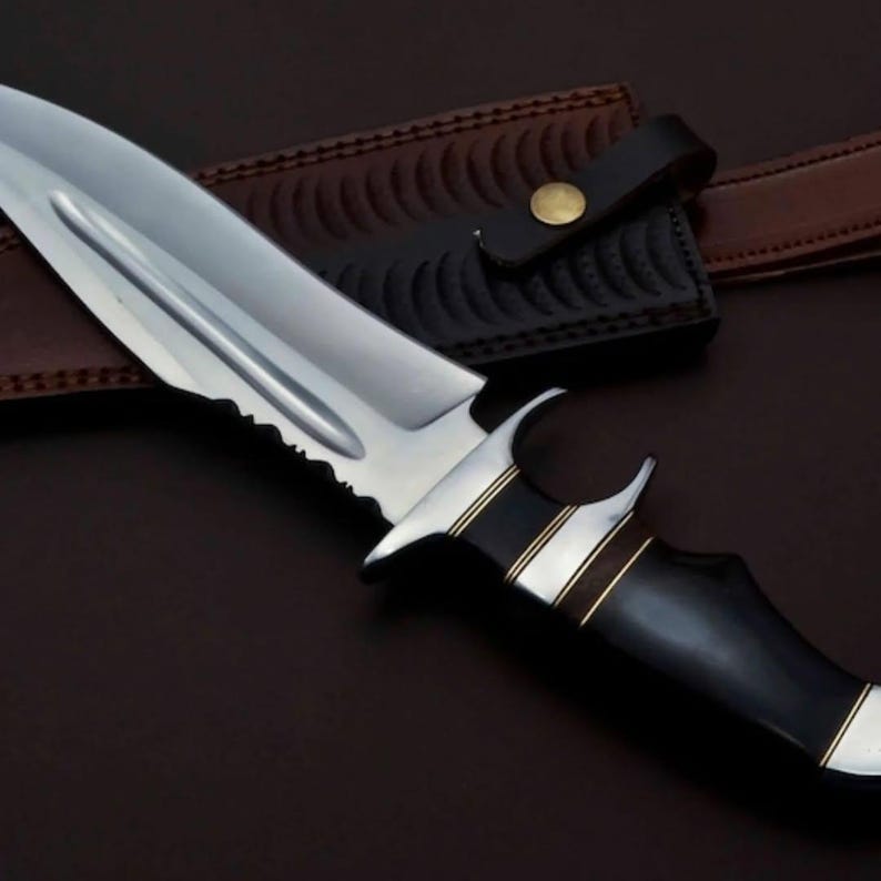 May include: A silver knife with a black handle and gold accents. The knife has a serrated edge and a leather sheath.