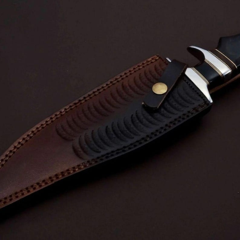 May include: A brown leather sheath with a black embossed pattern and a brass button. The sheath is designed to hold a knife.