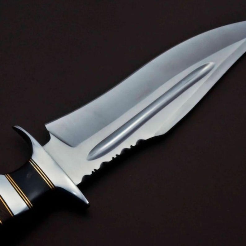 May include: A silver knife with a black and gold handle. The blade has a serrated edge and a pointed tip.