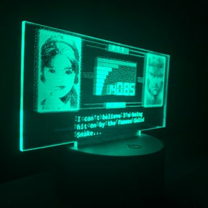 May include: A green LED light with a pixelated image of a woman and a man. The text "I can't believe I'm being hit on by the famous Solid Snake..." is displayed below the images.