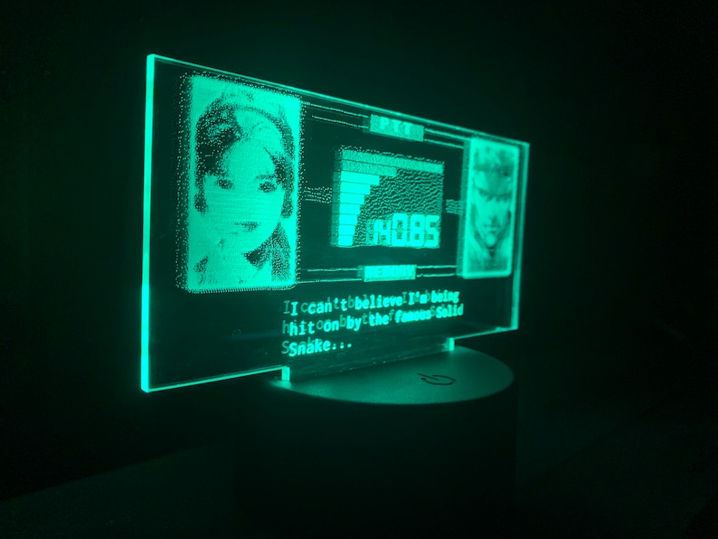 May include: A green LED light with a pixelated image of a woman and a man. The text "I can't believe I'm being hit on by the famous Solid Snake..." is displayed below the images.