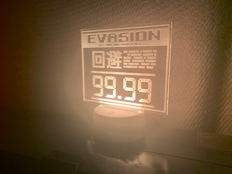 May include: A white acrylic sign with the word "EVASION" and a pixelated QR code. The sign also displays the price "99.99".