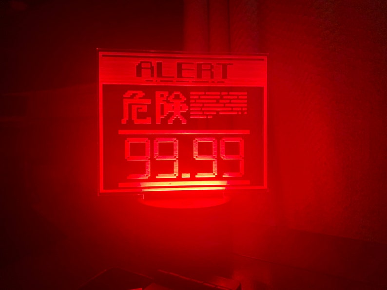 May include: A red LED sign with the word "ALERT" and the text "99.99" in a digital font. The sign is lit up and has a red glow.