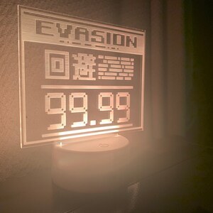 May include: A white acrylic sign with the word "EVASION" and a pixelated image of a square with a circle inside, and the number "99.99" displayed in a pixelated font.