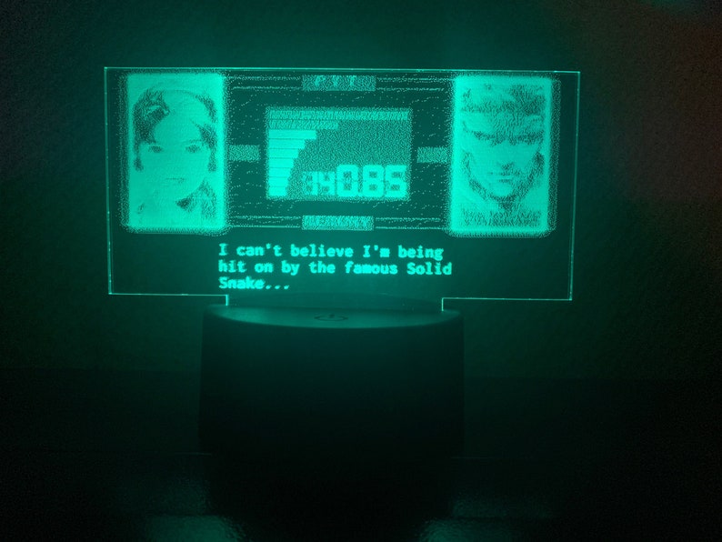 May include: A green LED light with a pixelated image of a video game character. The image is surrounded by a black border and includes the text "I can't believe I'm being hit on by the famous Solid Snake..."
