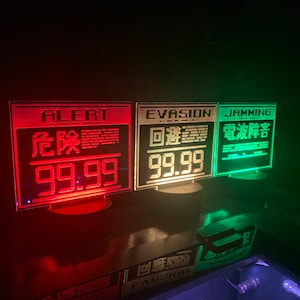 May include: Three red, white, and green illuminated signs with black text. The first sign reads "ALERT" in white, "危险" in red, and "99.99" in red. The second sign reads "EVASION" in white, "迴避" in white, and "99.99" in white. The third sign reads "JAMMING" in white, "電波干渉" in white, and "99.99" in white.