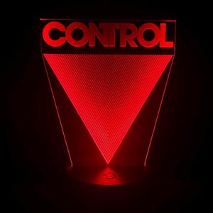 May include: A red LED night light shaped like a triangle with the word "CONTROL" in white letters at the top. The light is on and illuminating the room.