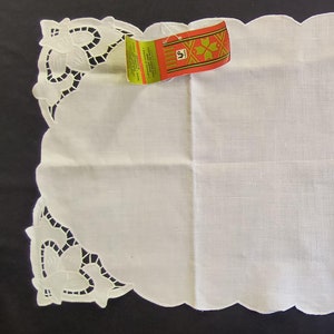 May include: White linen table runner with scalloped edges and cut-out floral corner designs. A colorful tag is attached to the corner. The runner is approximately 18 inches wide and 36 inches long.