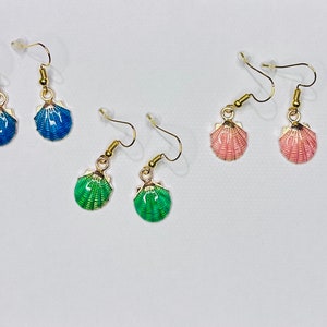 Peut inclure: Trois paires de boucles d'oreilles pendantes avec des crochets dorés et des breloques en forme de coquillages. Les coquillages sont bleus, roses et verts.