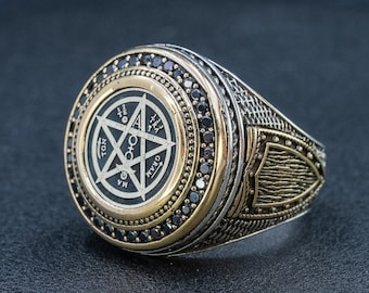 May include: A silver and gold ring with a black pentagram design and black stones around the edge. The pentagram has the words "TON", "MA", "GO", "HYN", and "OH" around it.