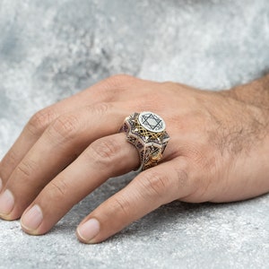 Puede incluir: Un anillo de plata con un dise&ntilde;o de estrella de David en oro. El anillo est&aacute; decorado con intrincados tallados y una piedra negra.