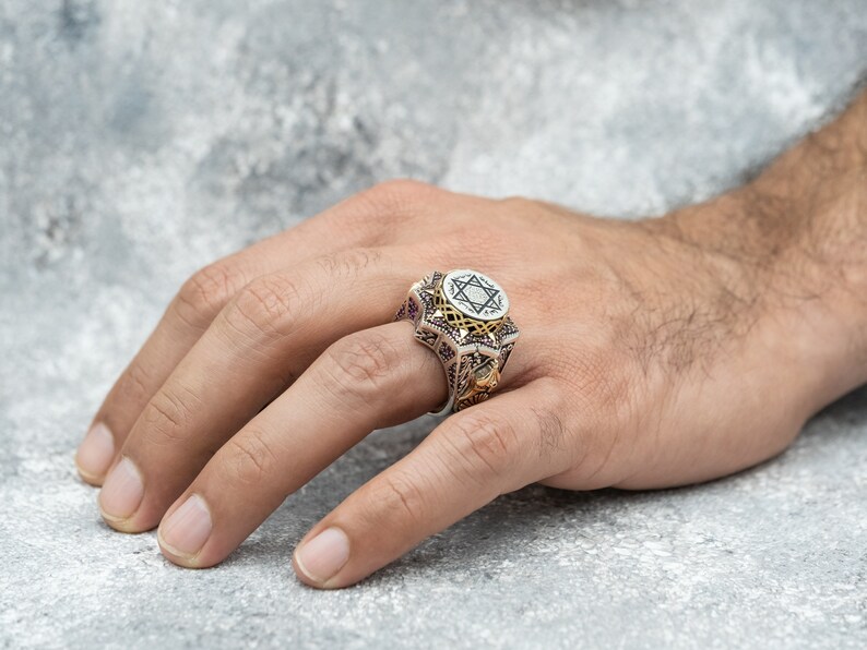 Puede incluir: Un anillo de plata con un dise&ntilde;o de estrella de David en oro. El anillo est&aacute; decorado con intrincados tallados y una piedra negra.