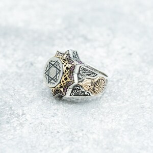 Puede incluir: Un anillo de plata con una estrella de David dorada y escritura &aacute;rabe en la cara. El anillo est&aacute; decorado con peque&ntilde;as piedras preciosas rosas y tiene un dise&ntilde;o detallado en la banda.