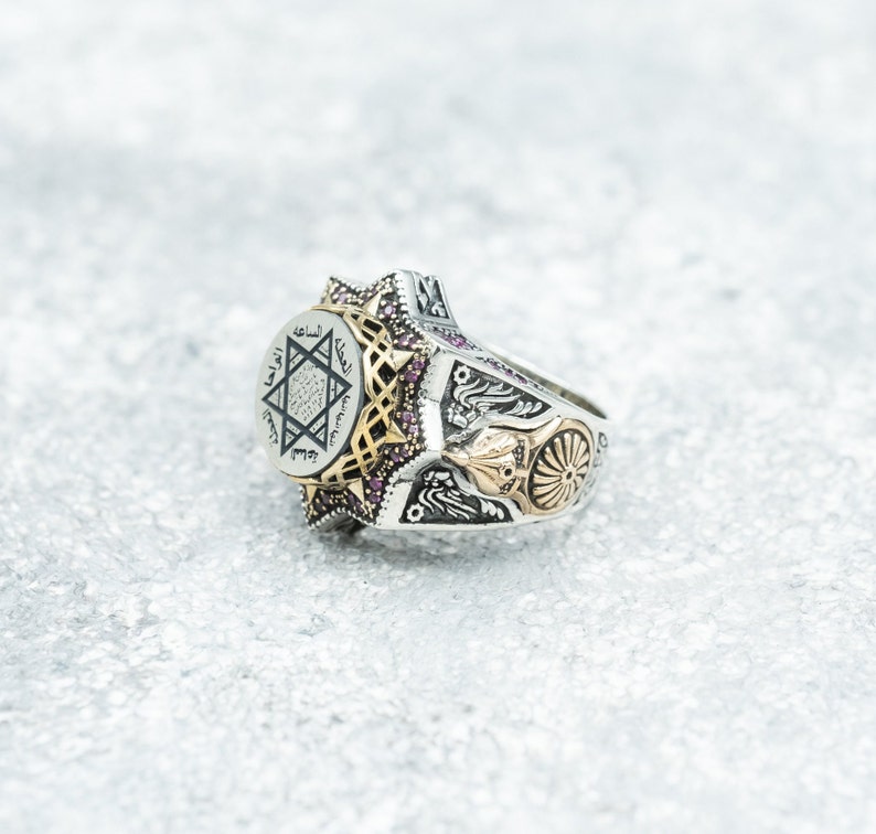 Puede incluir: Un anillo de plata con una estrella de David dorada y escritura &aacute;rabe en la cara. El anillo est&aacute; decorado con peque&ntilde;as piedras preciosas rosas y tiene un dise&ntilde;o detallado en la banda.