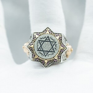 Puede incluir: Un anillo de plata y oro con un dise&ntilde;o de estrella de David y escritura &aacute;rabe. El anillo est&aacute; engastado con peque&ntilde;as piedras preciosas rosas.