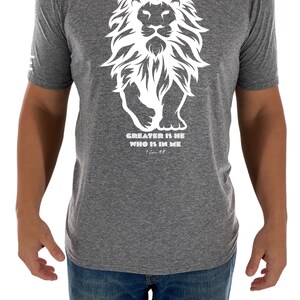 May include: A heather grey t-shirt with a white graphic of a lion with the text "GREATER IS HE WHO IS IN ME" and the scripture reference "1 John 4:4".