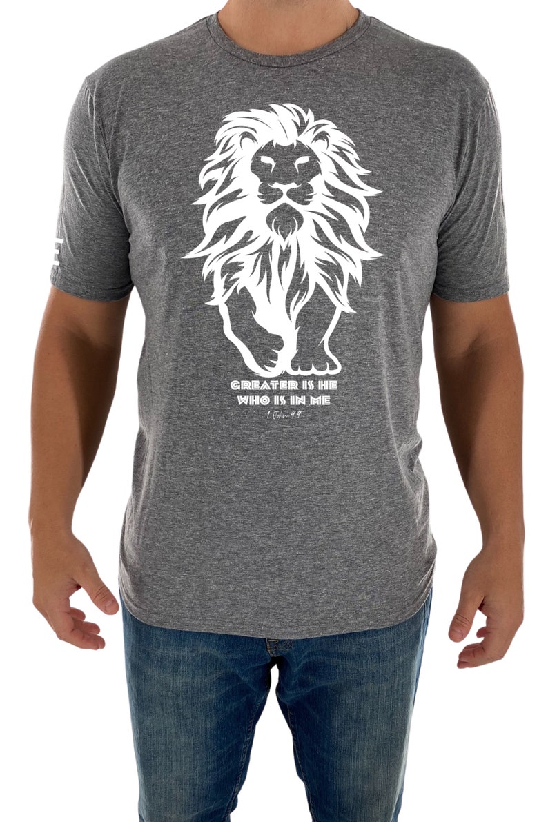 May include: A heather grey t-shirt with a white graphic of a lion with the text "GREATER IS HE WHO IS IN ME" and the scripture reference "1 John 4:4".