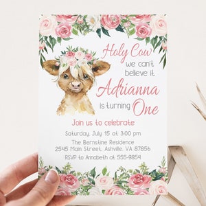 May include: A pink and white floral birthday invitation with a watercolor illustration of a Highland cow wearing a flower crown. The text reads "Holy Cow we can't believe it Adrianna is turning One. Join us to celebrate Saturday, July 15 at 3:00 pm The Bernstine Residence 2545 Main Street, Ashville, VA 87856 RSVP to Annabeth at 555-9854"