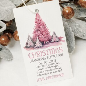 May include: A white tag with a pink Christmas tree design and the words "CHRISTMAS SIMMERING POTPOURRI" in pink. The tag includes instructions and the signature "LOVE. ANNEMARIE". The tag is attached to a string.