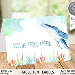 May include: Table tent labels with a watercolor background featuring a blue whale swimming in the ocean. The labels are 3.5 inches by 2.5 inches when folded and have the text "YOUR TEXT HERE" printed on them.