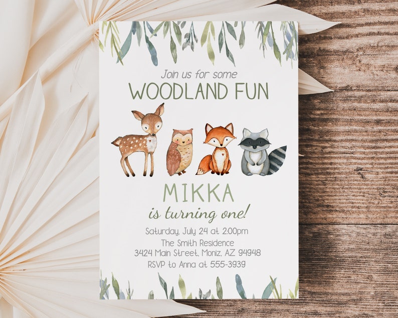 May include: A woodland-themed invitation with watercolor illustrations of a deer, owl, fox, and raccoon. The text reads "Join us for some WOODLAND FUN" and "MIKKA is turning one!" with event details. Green foliage accents the top and bottom.