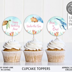 May include: Three cupcake toppers featuring an under the sea theme. The toppers are 2 inches in diameter and feature a sea turtle, a clownfish, and a whale. The toppers are printed on white cardstock and have a watercolour effect.
