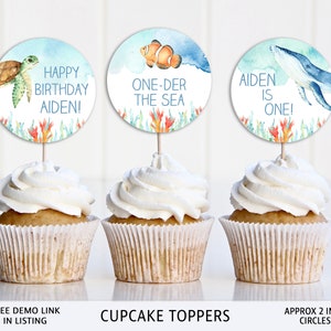 May include: Three cupcake toppers with watercolor illustrations of a turtle, a clownfish, and a whale. The toppers are decorated with coral and seaweed. The text on the toppers reads "Happy Birthday Aiden!", "One-der the Sea", and "Aiden is One!" The toppers are approximately 2 inches in diameter.