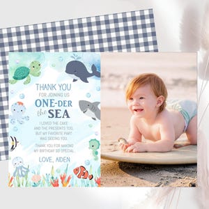 The image is a birthday card for a baby, featuring a beach scene with a baby lying on a surfboard and surrounded by sea creatures. The card also includes a photo of a smiling baby.