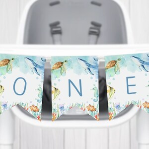 May include: A blue and white banner with the word "ONE" in blue letters. The banner features a watercolor design of sea creatures, including sea turtles, whales, seahorses, and fish.