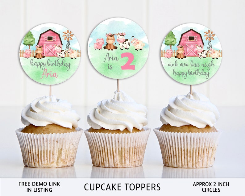May include: Three cupcake toppers with farm animal designs. The toppers are 2 inches in diameter and feature a pink barn, green grass, and farm animals. The text on the toppers reads "happy birthday Aria", "Aria is 2", and "oink moo baa neigh happy birthday".
