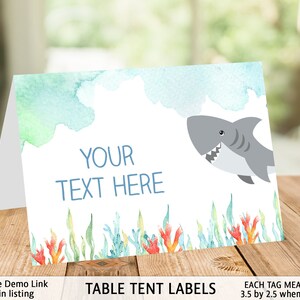 May include: Table tent labels with a watercolor background featuring a shark swimming in the ocean. The labels are 3.5 inches by 2.5 inches when folded and have the text "YOUR TEXT HERE" in blue.