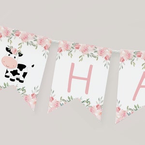 以下が含まれることがあります： ピンクとグリーンの花柄の横断幕に、ピンクの文字で「HA」と書かれています。横断幕には、ピンクの花冠をかぶった白黒の牛も描かれています。
