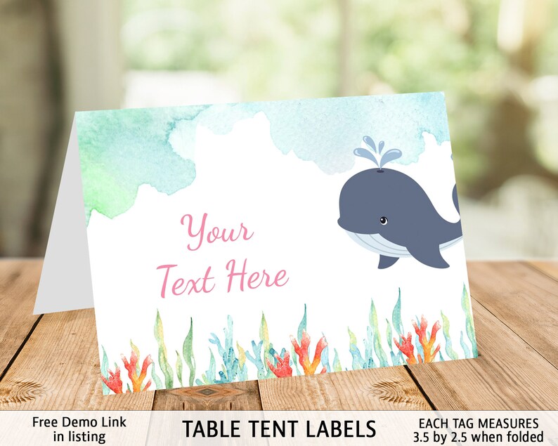 May include: Table tent labels with a watercolor design featuring a blue whale with a water spout, green and blue seaweed, and coral. The text "Your Text Here" is in pink. Each tag measures 3.5 inches by 2.5 inches when folded.