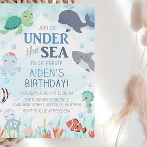 May include: Under the Sea themed birthday party invitation with a blue watercolor background. The invitation features cartoon sea creatures like a turtle, whale, octopus, shark, seahorse, and a clownfish. The text reads "Join us Under the Sea to celebrate Aiden's Birthday! Saturday, June 5 at 11:30 AM The Buckner Residence 2545 Main Street, Anisville, VA 87856 RSVP to Allie at 555-9854"