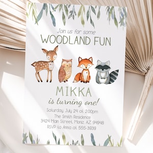 May include: A white invitation card with watercolor illustrations of woodland animals: a deer, owl, fox, and raccoon. The text reads "Join us for some WOODLAND FUN" and "MIKKA is turning one!" with event details.